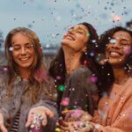 Four women at a break-up party throw confetti in the air and laugh