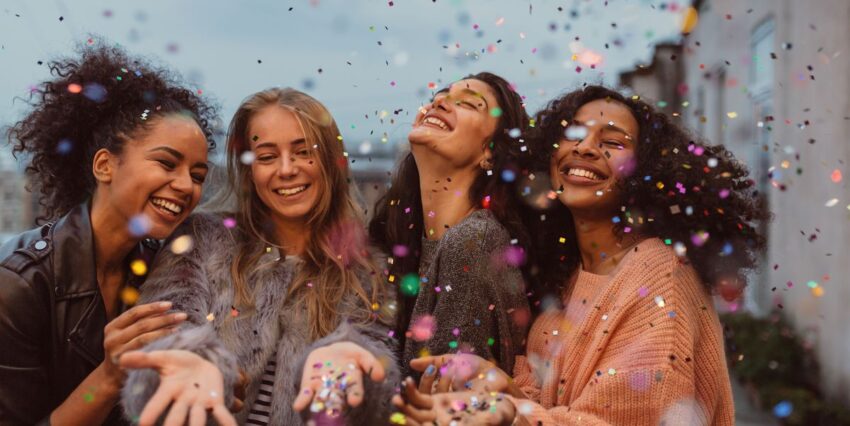 Four women at a break-up party throw confetti in the air and laugh