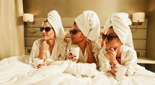Three women having a spa themed breakup party sitting on a bed with their hair wrapped in towels drinking tea